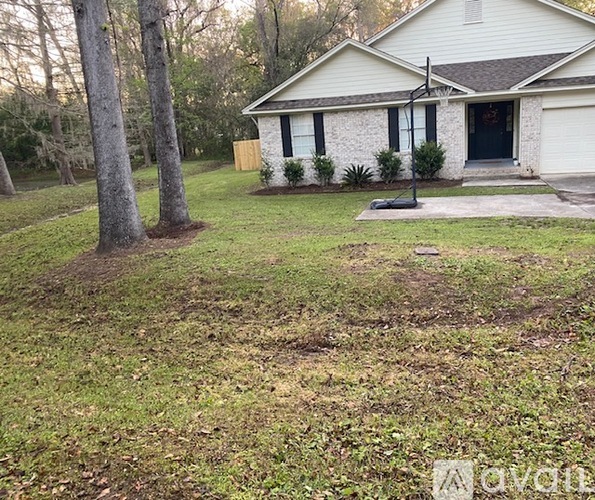 A house with a white exterior and a black door is surrounded by a grassy yard.