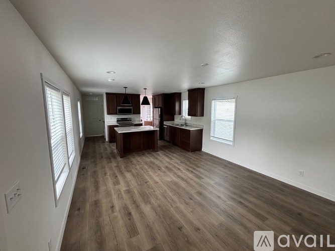 A spacious room with wooden flooring and a kitchen area in the background.