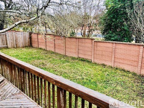 A wooden deck overlooks a grassy area with a red brick wall.