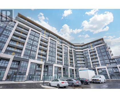 A modern building with a glass facade and a parking lot in front.