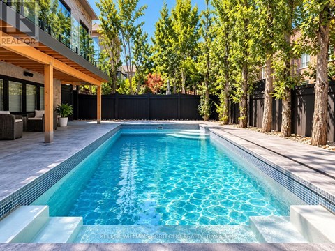 A swimming pool in a backyard with a wooden deck and a black fence.