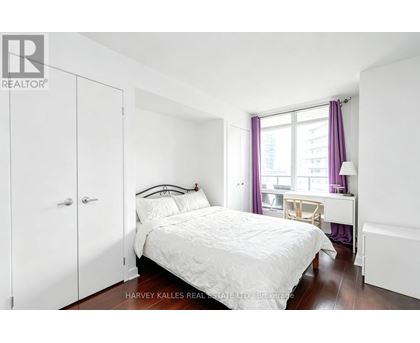 A bedroom with a white bed and a window with purple curtains.