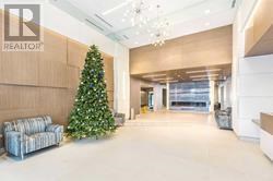A Christmas tree is in a living room with a couch and a chandelier.