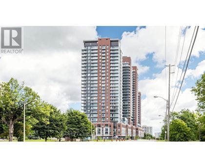 A tall residential building with a red brick facade stands in front of a row of trees.