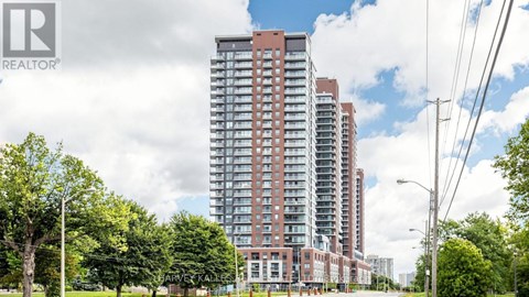 A tall residential building with a red brick facade stands in front of a row of trees.