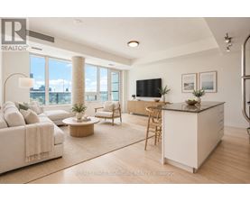 A well-lit, spacious living room with a large window, a sofa, a coffee table, and a kitchen area.