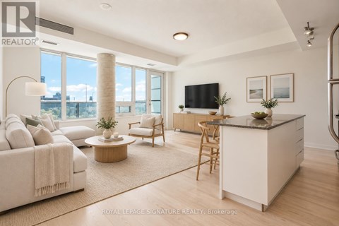 A well-lit, spacious living room with a large window, a sofa, a coffee table, and a kitchen area.
