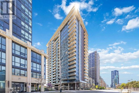 A tall, modern building with a glass facade stands in the foreground of a city street.