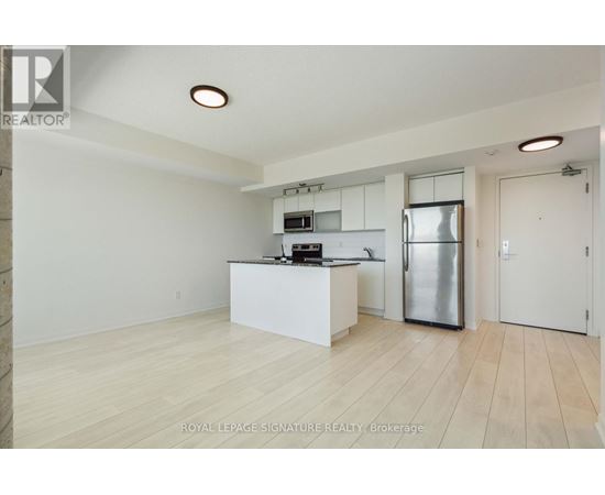 A kitchen with white cabinets and a refrigerator in a room with wooden flooring.