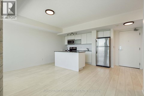 A kitchen with white cabinets and a refrigerator in a room with wooden flooring.
