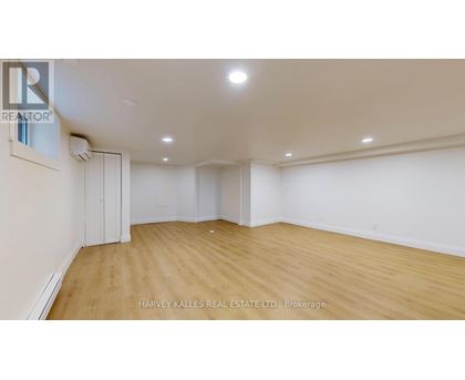 A spacious room with wooden flooring and white walls, with a realtor logo on the wall.