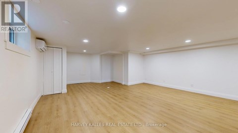 A spacious room with wooden flooring and white walls, with a realtor logo on the wall.