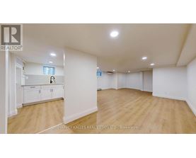 A spacious room with wooden flooring and white walls, with a cabinet and a window.