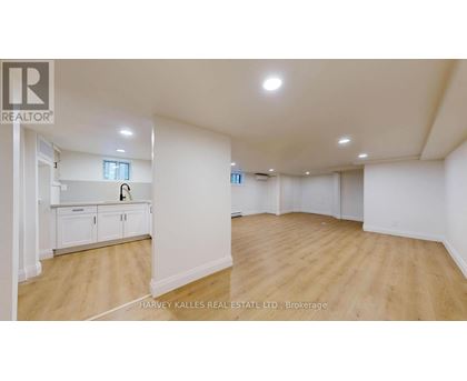 A spacious room with wooden flooring and white walls, with a cabinet and a window.