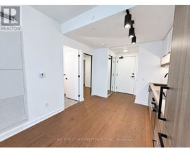 A spacious room with wooden flooring and white walls, with a staircase on the right side.