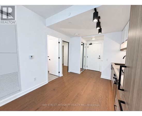 A spacious room with wooden flooring and white walls, with a staircase on the right side.
