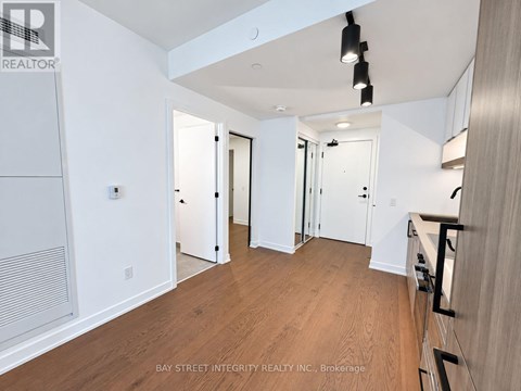 A spacious room with wooden flooring and white walls, with a staircase on the right side.