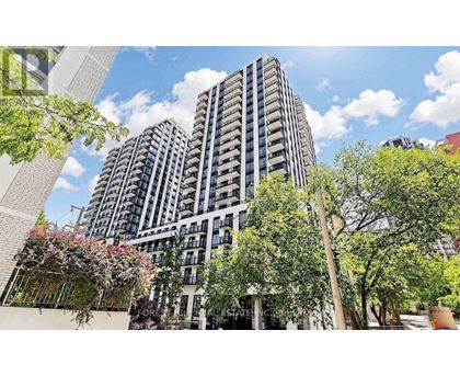 A modern building with a lot of windows and balconies is surrounded by trees and plants.