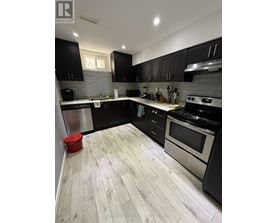 A modern kitchen with black cabinets and a wooden floor.