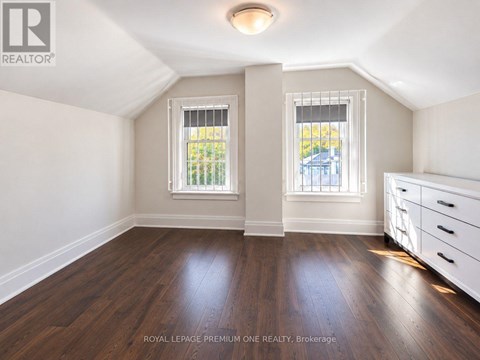 A room with wooden floors and white walls, with a window showing a view of a blue building.