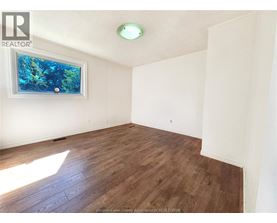 A room with wooden flooring and a window showing trees outside.