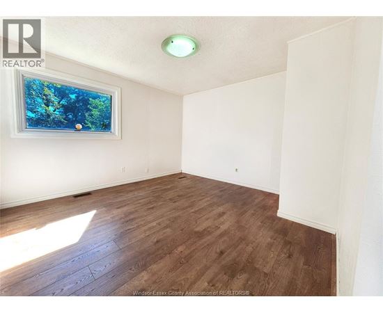 A room with wooden flooring and a window showing trees outside.