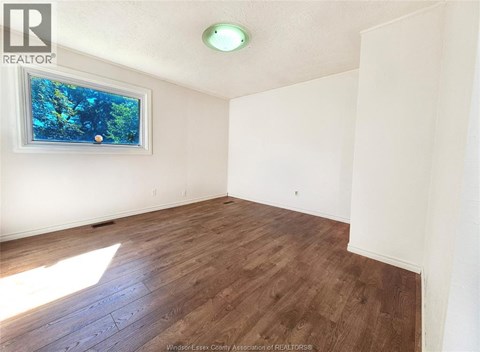 A room with wooden flooring and a window showing trees outside.
