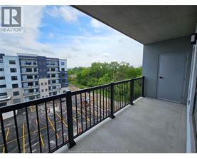 A balcony with a black railing and a view of a parking lot and trees.
