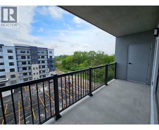A balcony with a black railing and a view of a parking lot and trees.