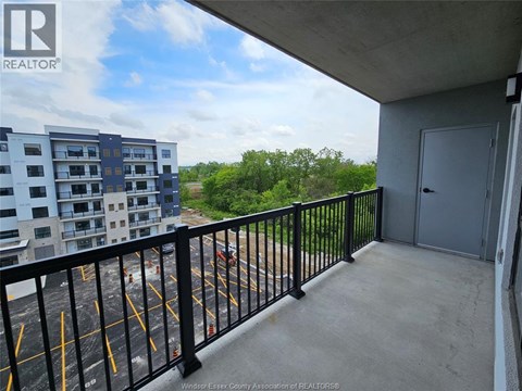 A balcony with a black railing and a view of a parking lot and trees.