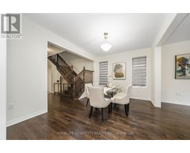 A spacious room with a dining table and chairs and a staircase in the background.