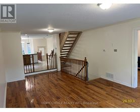 A spacious room with wooden floors and a staircase.