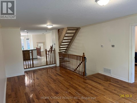 A spacious room with wooden floors and a staircase.