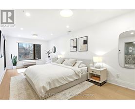 A bedroom with a large bed and a window overlooking a tree-lined street.