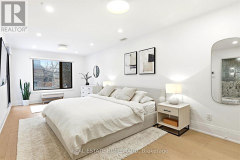 A bedroom with a large bed and a window overlooking a tree-lined street.