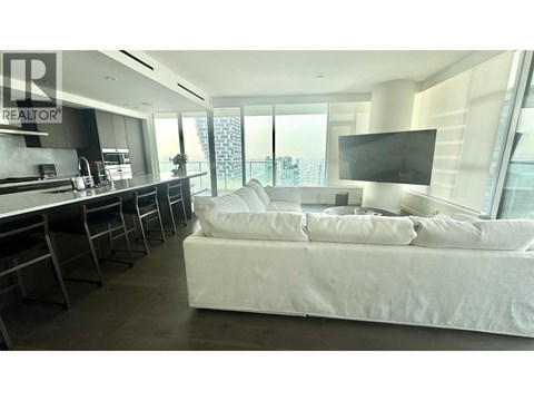 A bedroom with a large bed and a kitchen area in the background.