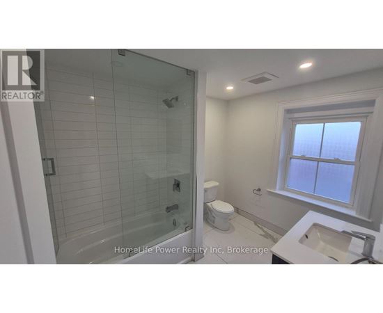A bathroom with a glass shower stall and a toilet next to a sink.