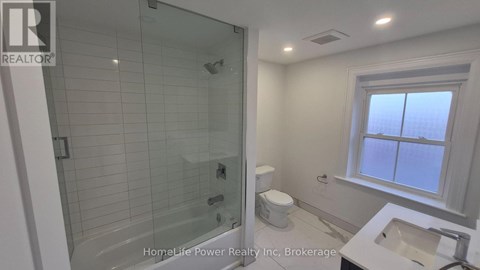 A bathroom with a glass shower stall and a toilet next to a sink.