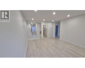 A spacious room with wooden flooring and white walls, with a door on the right and a window on the left.