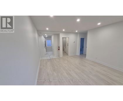 A spacious room with wooden flooring and white walls, with a door on the right and a window on the left.