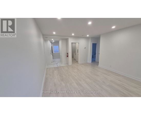 A spacious room with wooden flooring and white walls, with a door on the right and a window on the left.