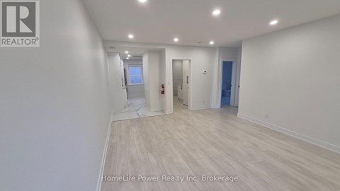 A spacious room with wooden flooring and white walls, with a door on the right and a window on the left.