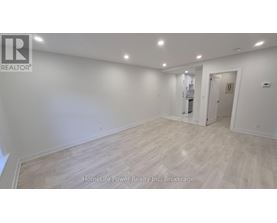 A spacious room with wooden flooring and white walls, with a door on the right side.