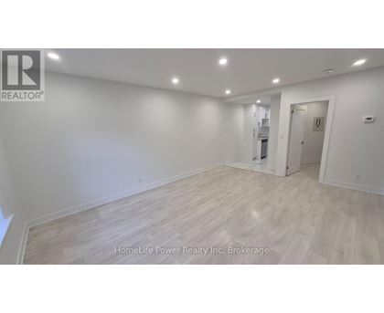 A spacious room with wooden flooring and white walls, with a door on the right side.