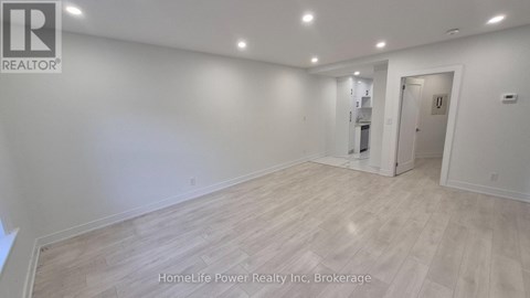 A spacious room with wooden flooring and white walls, with a door on the right side.