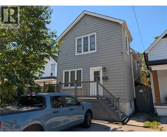 A silver truck is parked in front of a grey house.