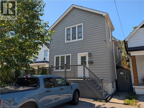 A silver truck is parked in front of a grey house.