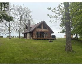 A wooden cabin with a porch and a chimney is surrounded by a grassy field.