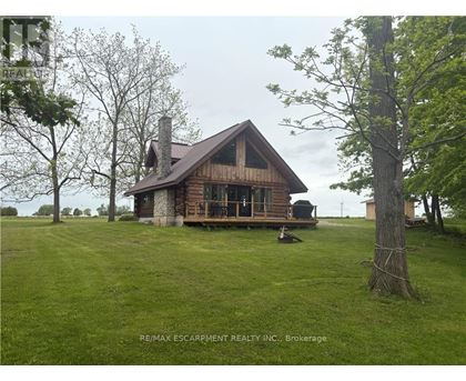 A wooden cabin with a porch and a chimney is surrounded by a grassy field.
