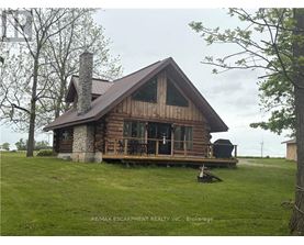 A wooden cabin with a stone chimney is surrounded by a grassy field.